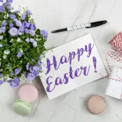 Wielkanocne słówka po angielsku: "Happy Easter!" na kartce, obok kwiatów, makaroników i prezentu.