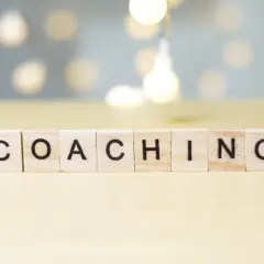 Drewniane klocki z literami układają słowo "COACHING". To właśnie kim jest coach – osoba wspierająca rozwój.